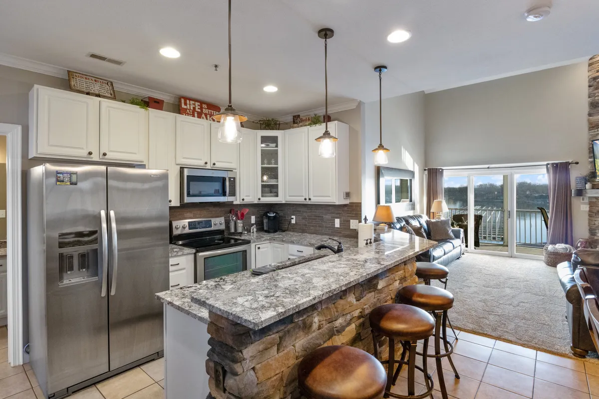 A warmly lit, open-concept kitchen featuring a spacious granite countertop, modern stainless steel appliances, and inviting bar stools. Large windows flood the space with natural light, creating a welcoming atmosphere ideal for group cooking and conversation.