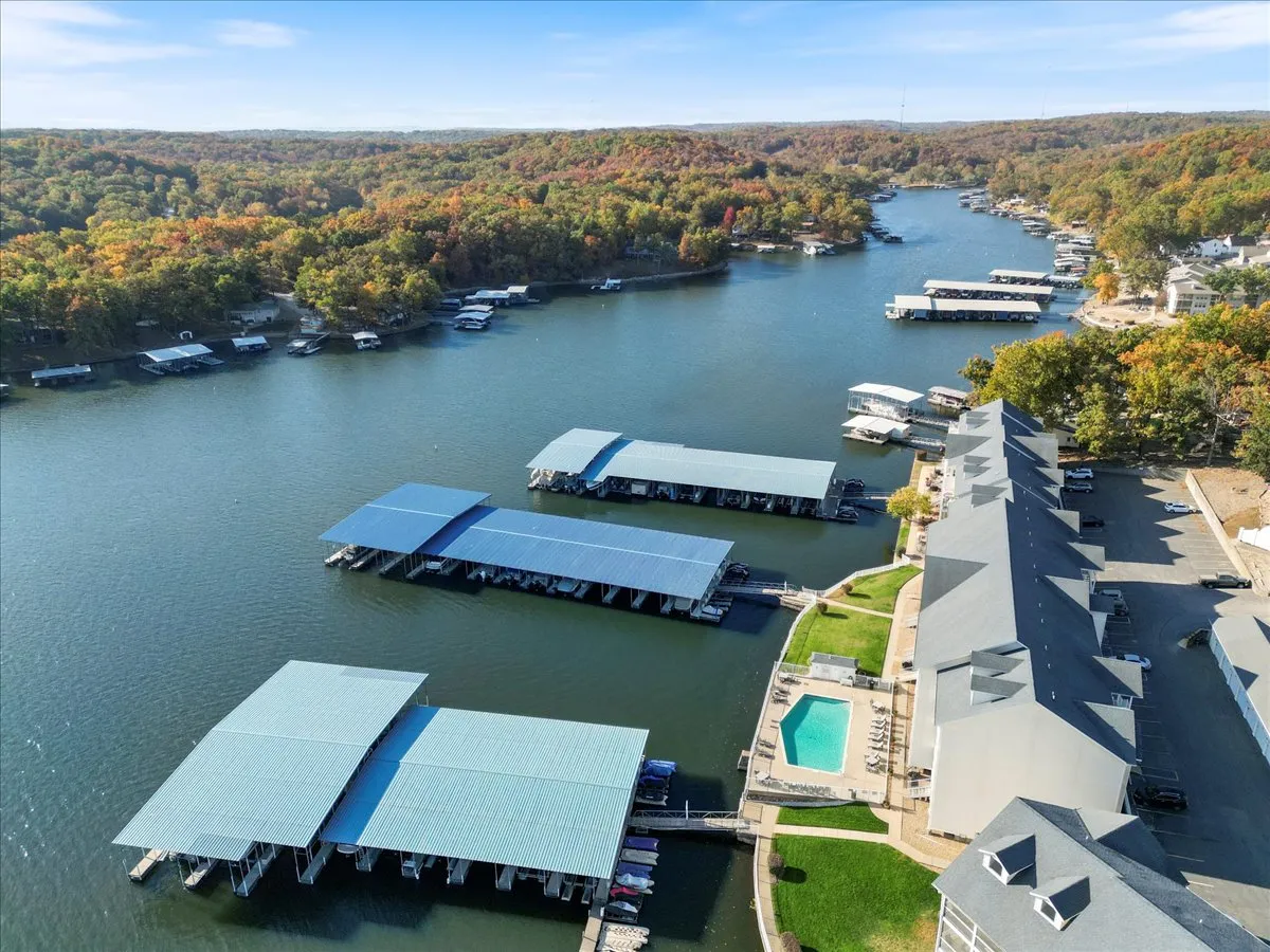 This wide exterior shot highlights the marina with boat docks, a swimming pool, colorful fall foliage, and the river, with residential buildings in the background. Activities like boating, fishing, swimming, and hiking are all visually suggested, broadening the sense of exploration and variety available to guests.