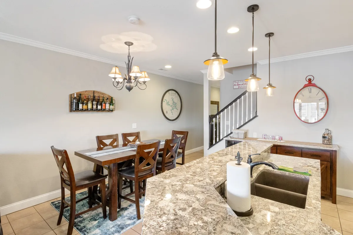 An adjacent dining area featuring a large wooden table, kitchen island, elegant chandelier, and a visible wine rack. The space is styled for both everyday meals and special occasions, encouraging family bonding and group gatherings.