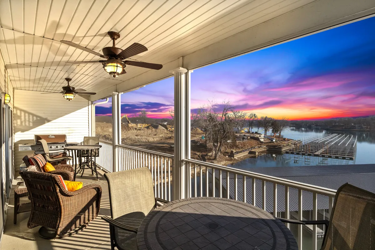 This exterior image captures an inviting outdoor seating area overlooking a panoramic waterfront view, with a grill and colorful sunset in the background. The mood is tranquil and inviting, perfect for gatherings and shared meals while immersed in nature.