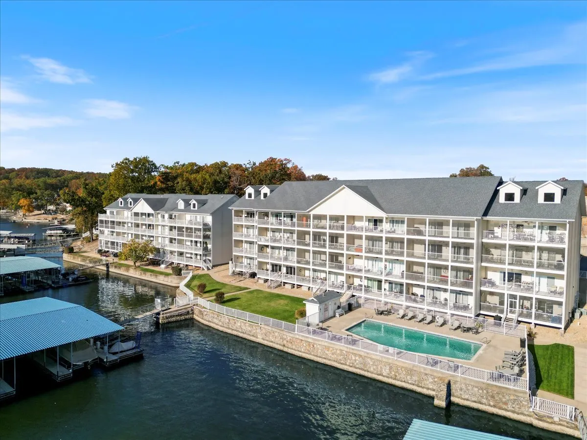 The image features a vibrant waterfront scene with a swimming pool, balconies, and boats docked in the marina. The view conveys a lively yet laid-back atmosphere, with easy access to the water and opportunities for boating and lakeside activities.
