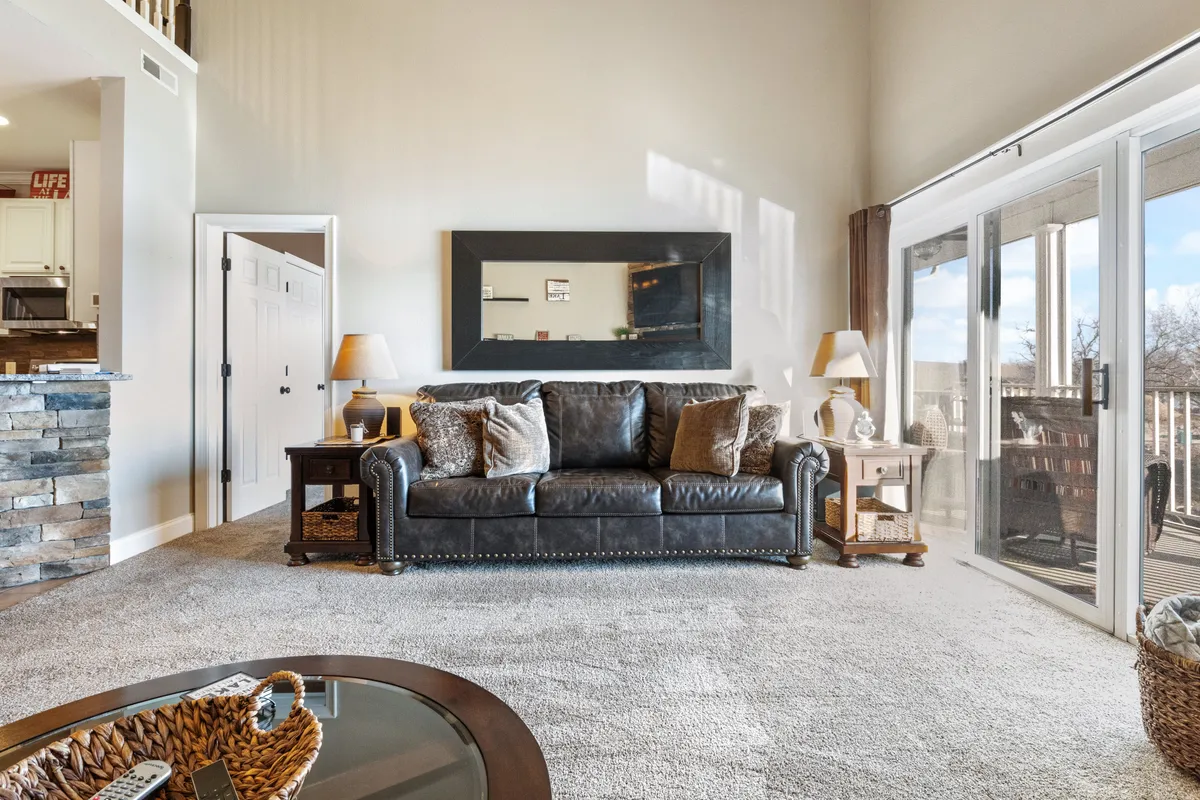 Inside, a cozy living area with a leather couch, large mirror, and sliding glass doors creates a welcoming atmosphere for relaxing or entertaining. The space is filled with natural light, hinting at the seamless transition between indoor comfort and outdoor beauty.