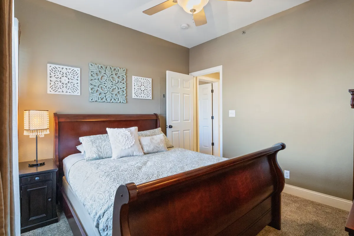 A tranquil bedroom scene showcases a comfortable bed, decorative wall art, a nightstand, and a lamp. The ample natural light and tasteful furnishings create an atmosphere of relaxation and privacy, offering a peaceful retreat after a day of activities.