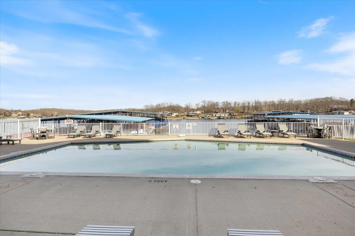 This image features a sparkling swimming pool, comfortable deck chairs for lounging, and a beautiful lake view in the background. The scene is lively, with the potential for swimming, sunbathing, socializing, and boating activities, epitomizing the lakeside lifestyle.