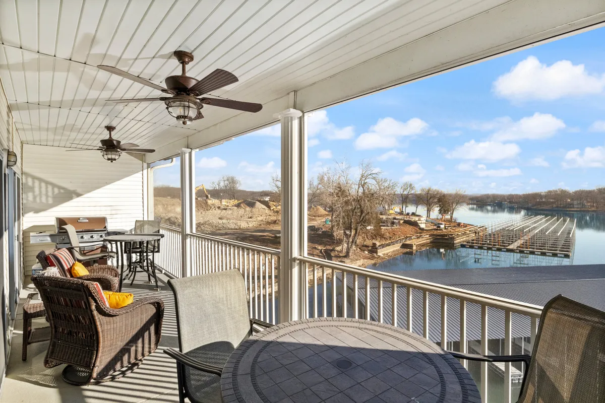 This image shows a spacious outdoor patio adorned with comfortable furniture and a grill, overlooking serene lake waters. Ceiling fans add comfort for outdoor gatherings, and the area is perfectly positioned to capture sunset views across the water.
