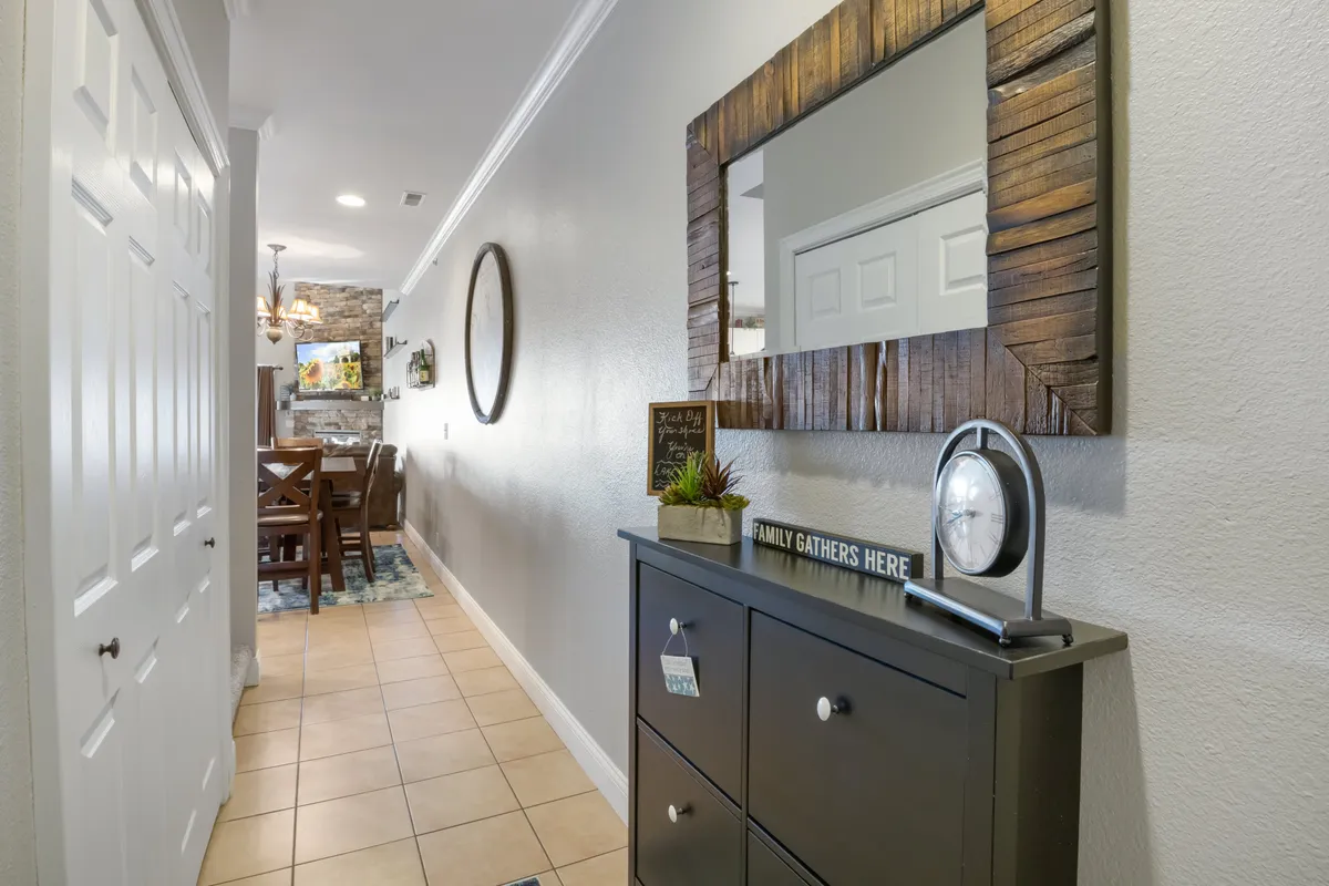 A console table with a mirror and a sign bearing a family motto creates a sense of arrival and personal welcome. The area is styled with decor elements that evoke warmth and a sense of belonging, ideal for greeting guests and enhancing the first impression.